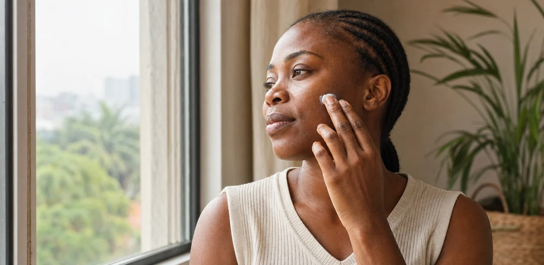 A Nigerian woman applying sunscreen beside a bright window in Lagos